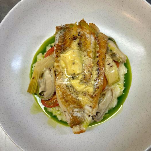 Pan Roasted Fish of the Day with risotto, cherry tomatoes, marinated artichoke, mussels, and hollandaise butter on a plate.