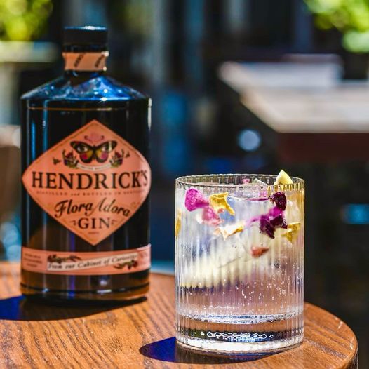 Hendrick's Gin in a glass with a slick's of lemon and edible flowers as garnish.