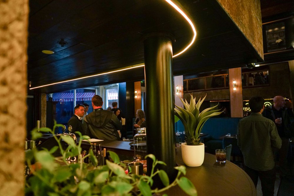 Image of a bar with greenery, plants, people in the background and an LED light.